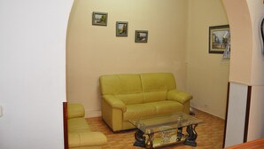 Una sala de estar con un sofá verde, una mesa de centro de vidrio y tres cuadros en la pared.