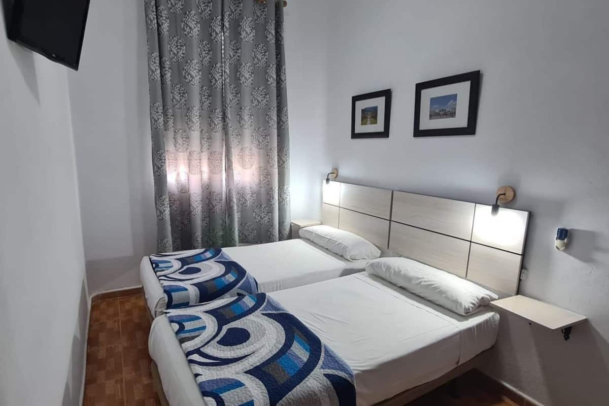 A double bed with a patterned blanket, a bedside table, a mounted TV, and two framed pictures on the wall.