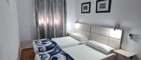 Una cama doble con una manta estampada, una mesita de noche, un televisor montado y dos cuadros en la pared.