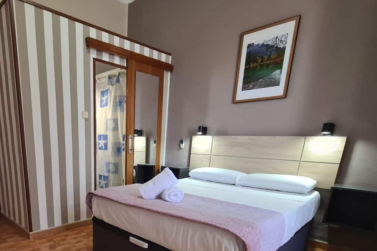 A hotel room with a bed, a headboard, a painting on the wall, and a striped curtain.