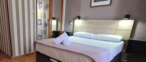 A hotel room with a bed, a headboard, a painting on the wall, and a striped curtain.