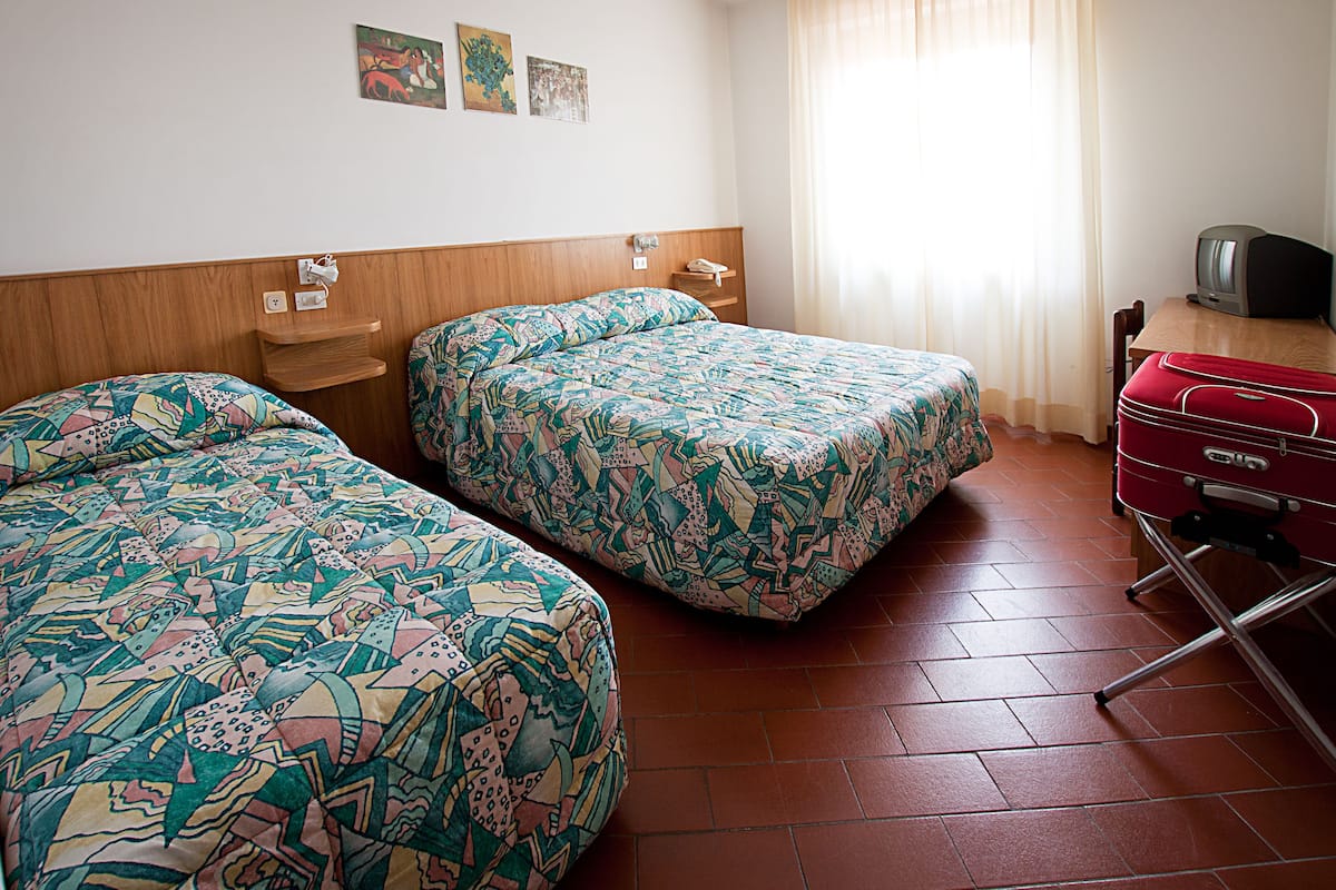 A hotel room with two beds, a wooden headboard, a red suitcase, and a television on a wooden table.