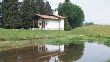 A small white church with a tiled roof, surrounded by a grassy field and a body of water reflecting its structure.