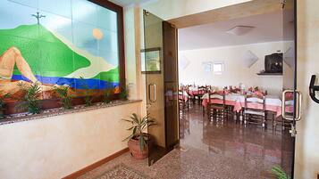 Un vestíbulo de hotel con un mural grande, una recepción y un comedor con mesas y sillas.