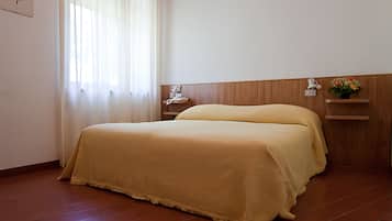 Une chambre d’hôtel avec un lit, une table de chevet, une étagère fixée au mur et une fenêtre avec des rideaux.