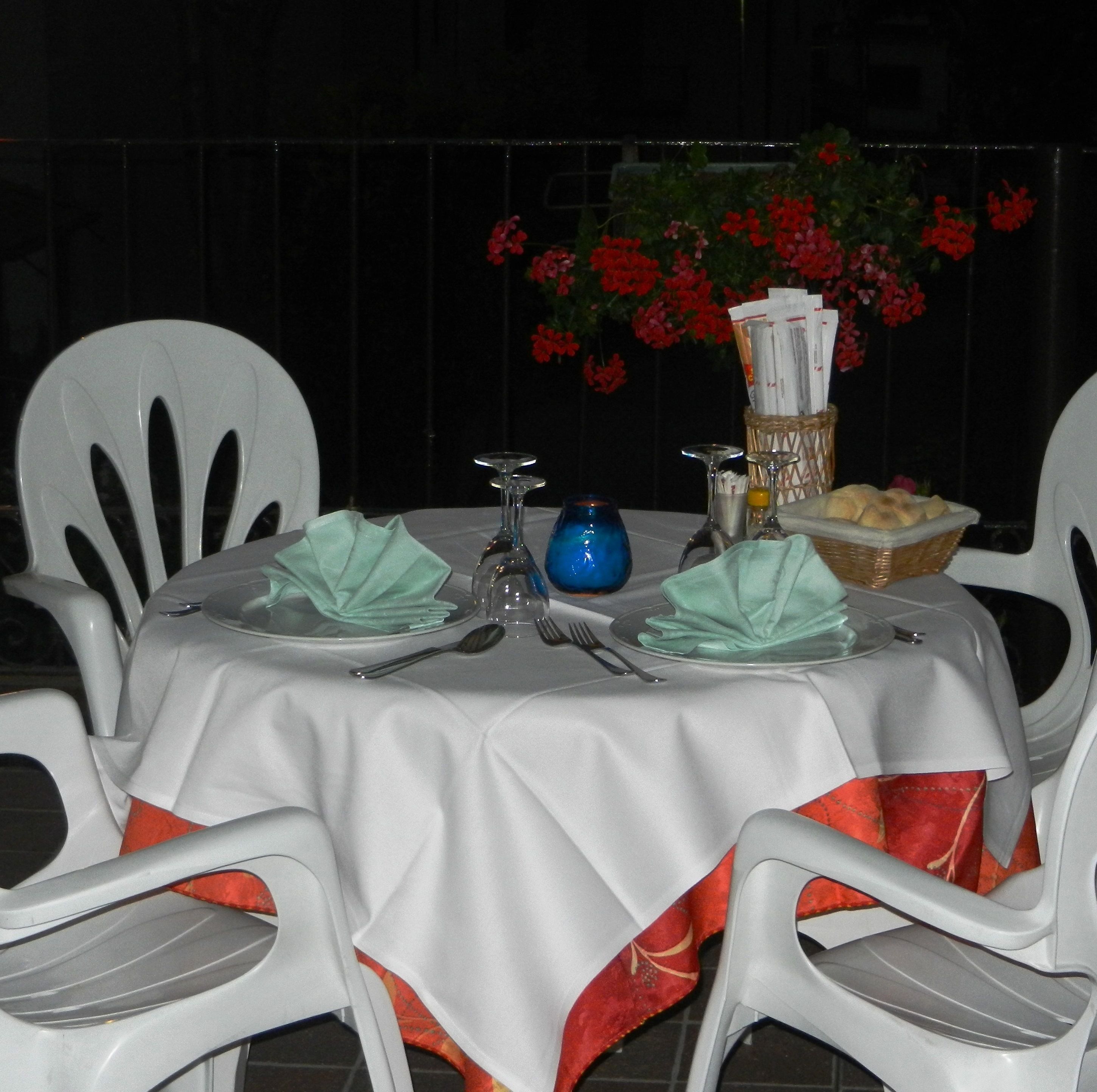 A table set for a meal with white chairs, a tablecloth, and a vase of red flowers.