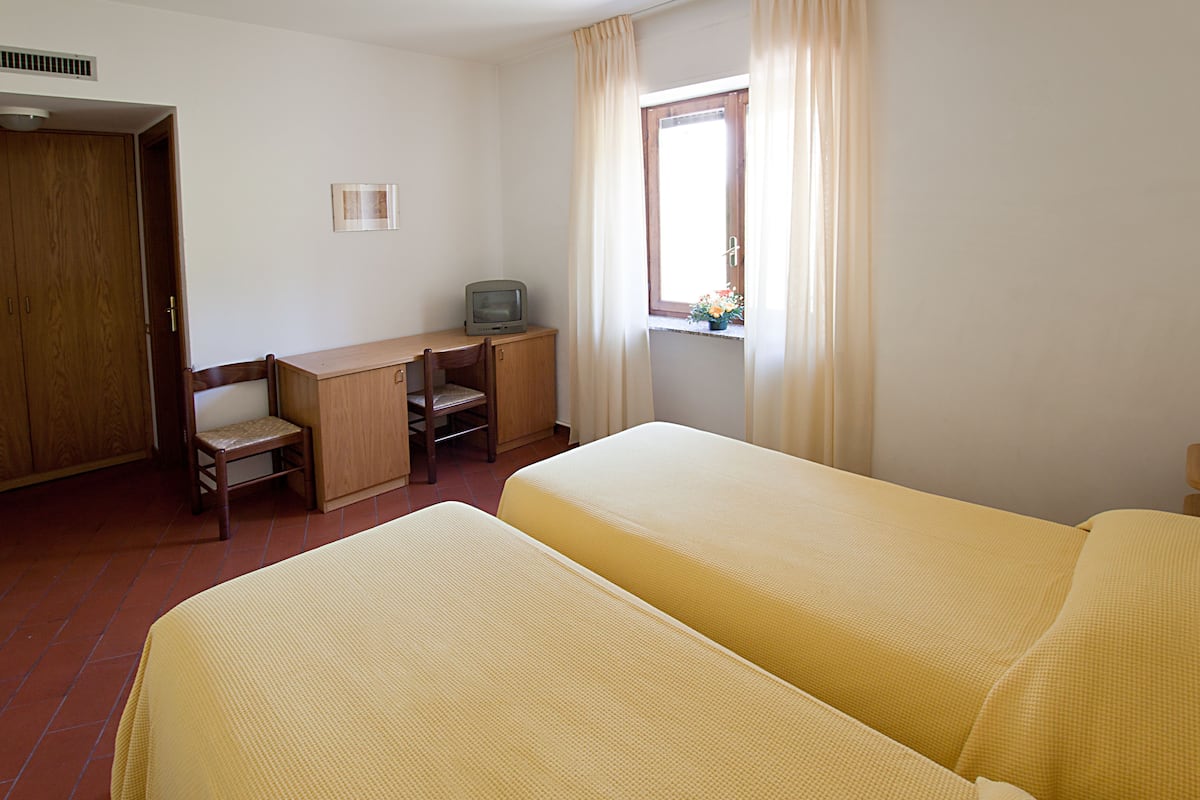 A room with two beds, a desk, a chair, a television, and a window with curtains.