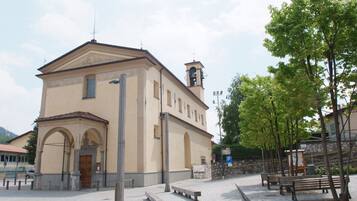 A building with a bell tower, a paved courtyard with benches, and a stone wall.