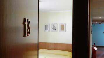 Una habitación de hotel con una cama, una puerta con un número y tres cuadros en la pared.