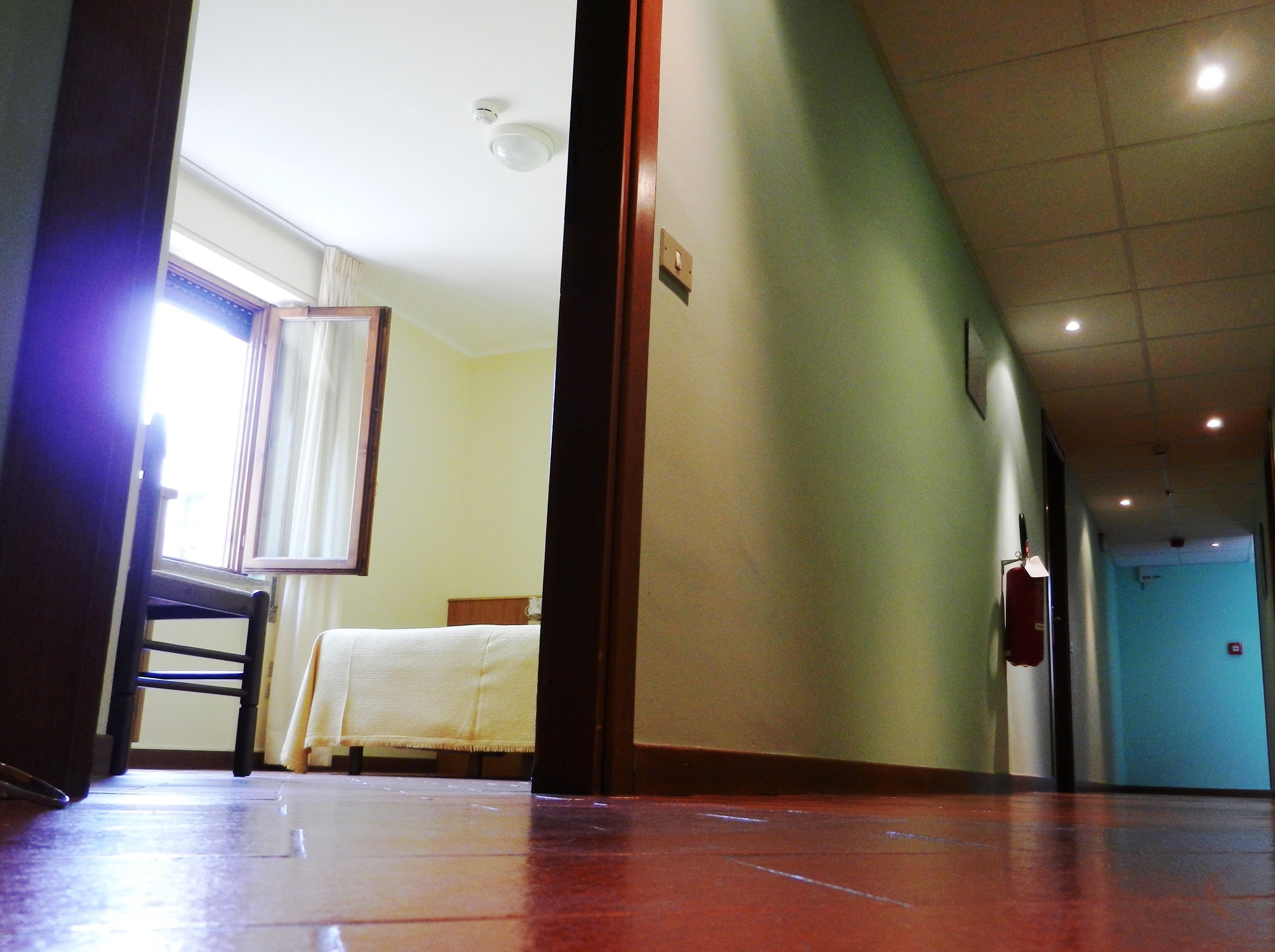 Un corridoio d'albergo con un letto, un estintore e una porta in fondo.