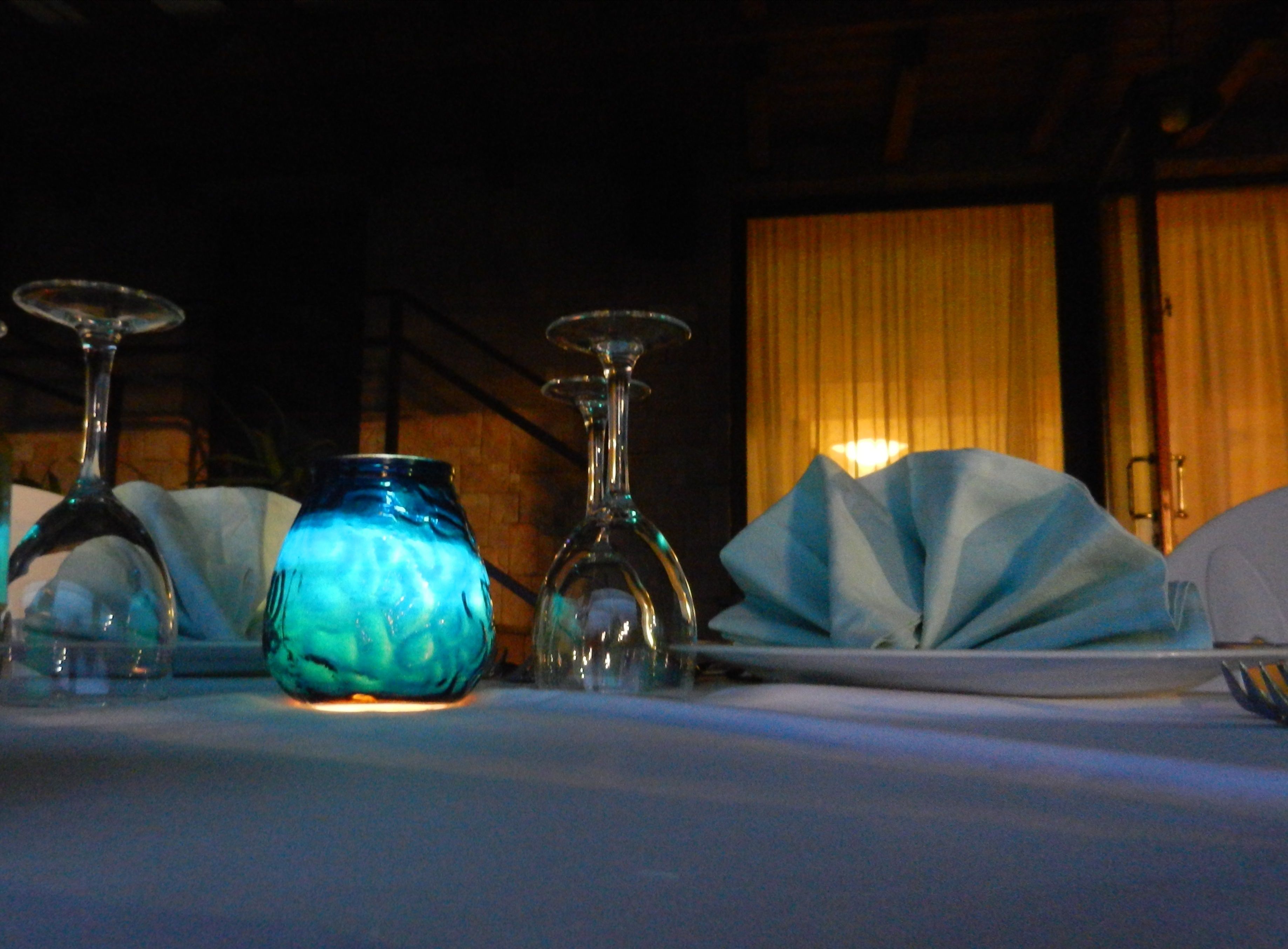 Ein gedeckter Tisch mit Glaswaren und einer blauen Vase, im Hintergrund eine Holztür und Vorhänge.