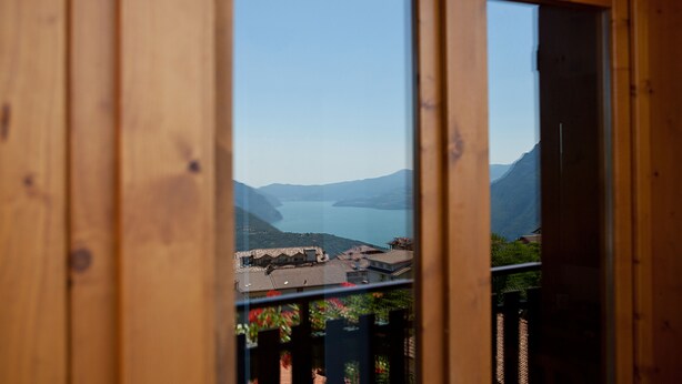 A wooden-framed window with a view of a lake and mountains. - Hotel Albergo Al Milano (Bossico)