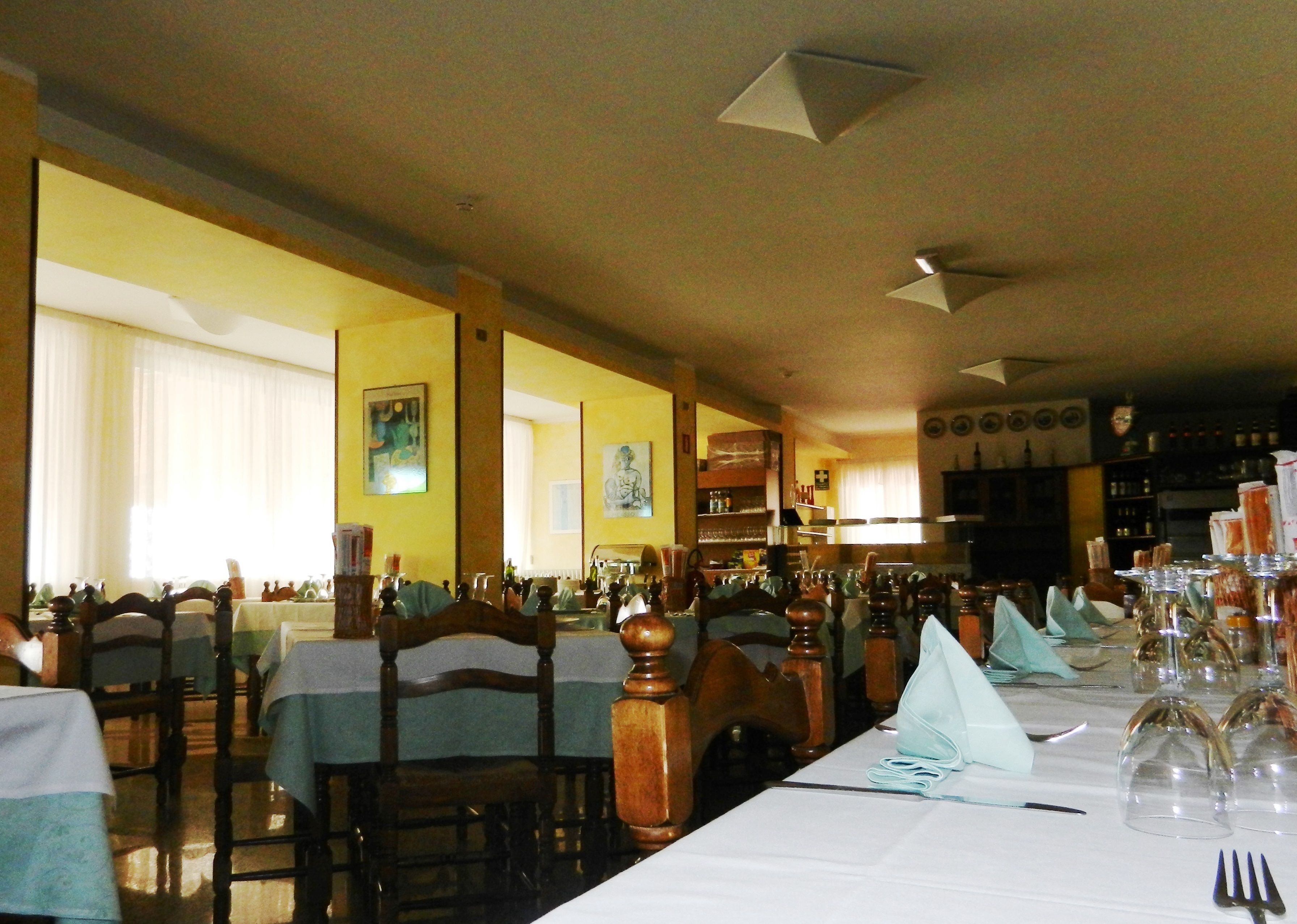 Un restaurante con varias mesas dispuestas para comer, sillas de madera y una zona de bar al fondo.