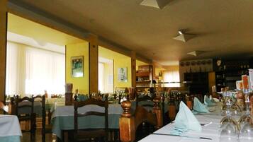 Un restaurante con varias mesas dispuestas para comer, sillas de madera y una zona de bar al fondo.