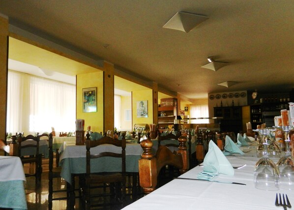 A restaurant with multiple tables set for dining, wooden chairs, and a bar area in the background.