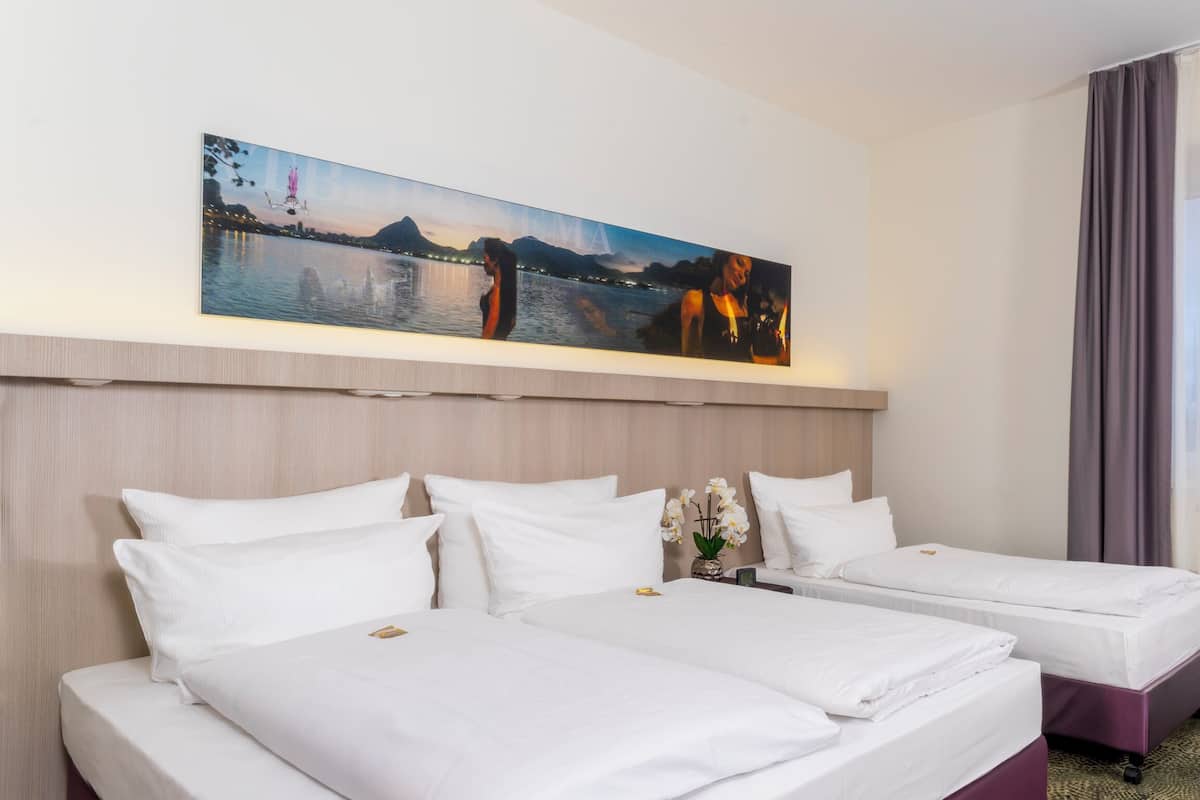 A hotel room with two beds, a large painting of a cityscape, and a view of a body of water.