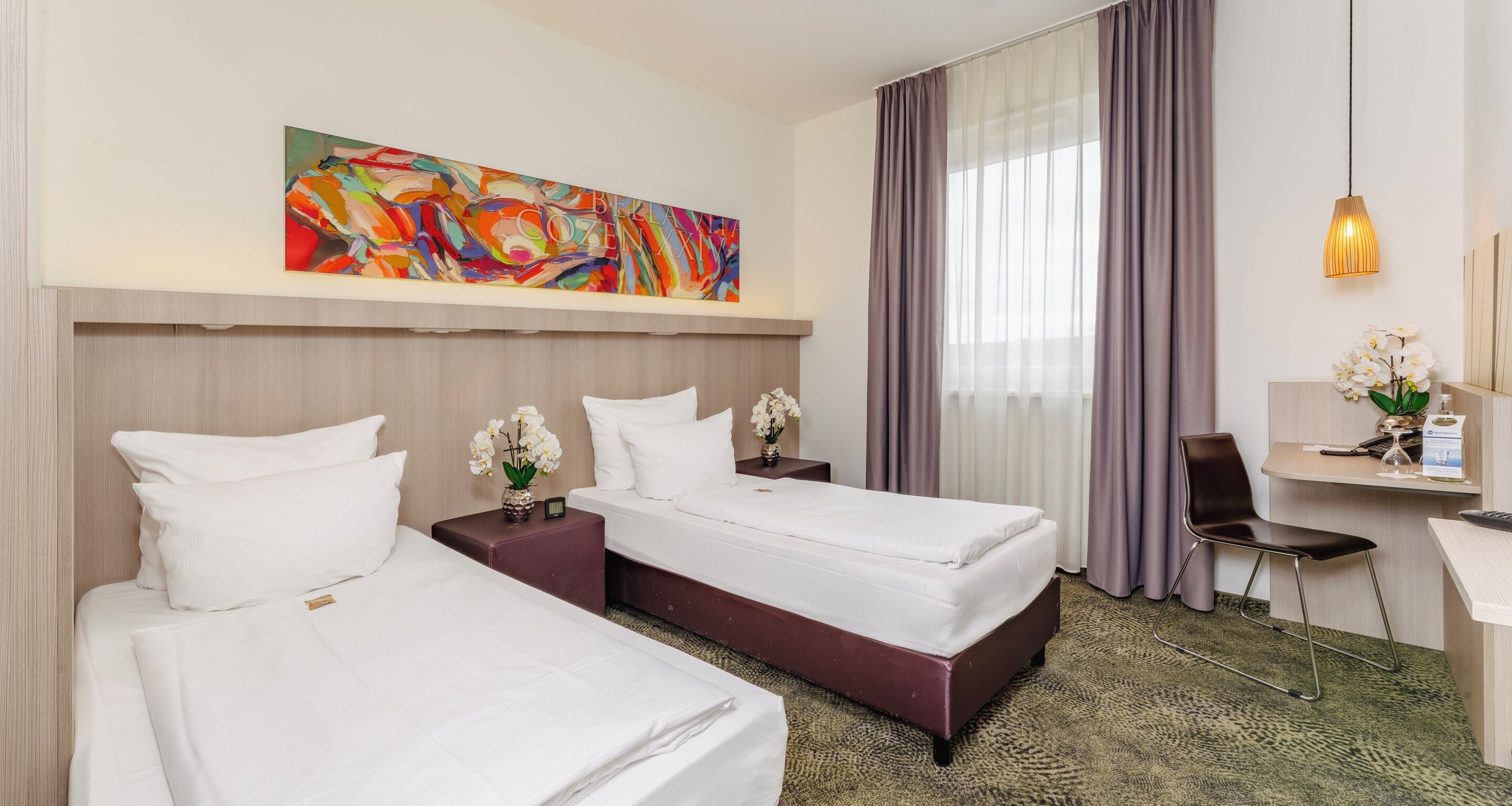 A hotel room with two beds, a desk, a chair, a painting, and a window with curtains.