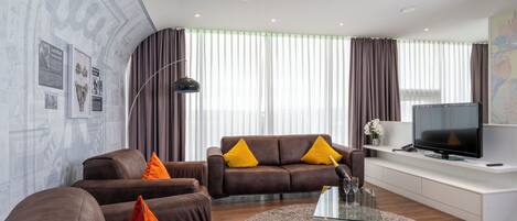 A modern living room with a brown leather sofa, a glass coffee table, and a flat-screen TV on a white console.