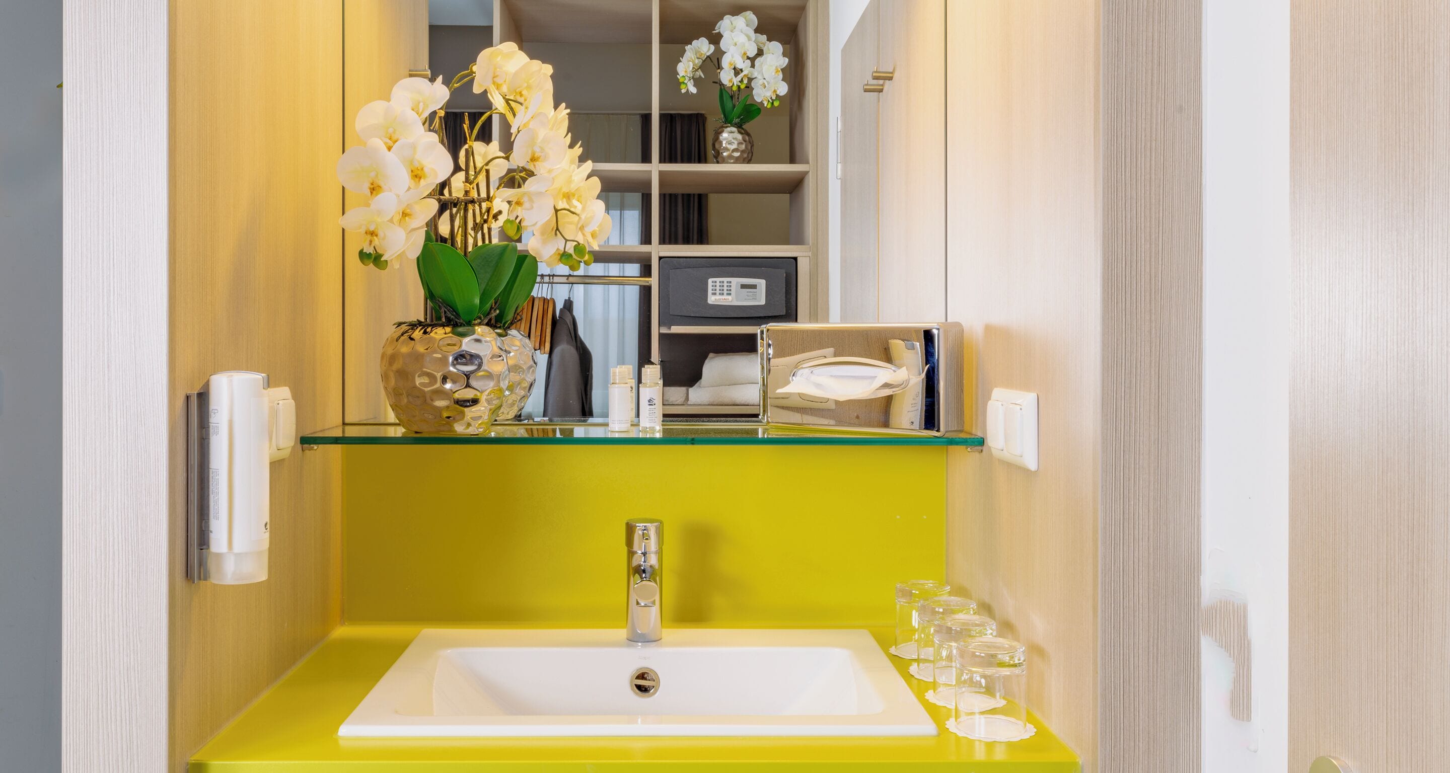 Un baño con un lavabo amarillo, un espejo y un jarrón con orquídeas blancas.