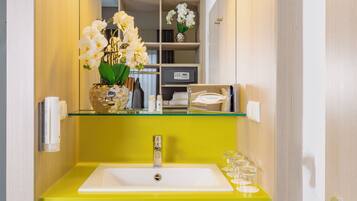 Un baño con un lavabo amarillo, un espejo y un jarrón con orquídeas blancas.