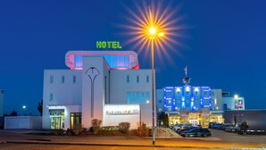 A hotel with a prominent 'HOTEL' sign, a parking lot, and a building with a clock tower in the background.