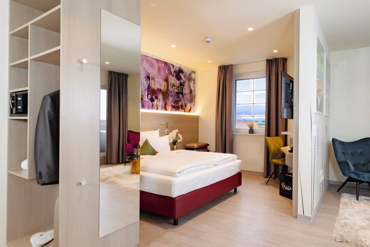 A modern hotel room with a large bed, a desk, a chair, and a view of the city.