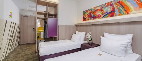 A hotel room with two beds, a large abstract painting, a wardrobe, and a small table with a vase of flowers.