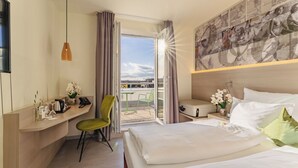 A hotel room with a bed, a desk with a chair, a TV, a window with curtains, and a balcony with chairs.