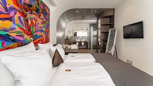 A hotel room with a large colorful abstract painting, a modern bathroom with a mirror and sink, and a flat-screen TV mounted on the wall.