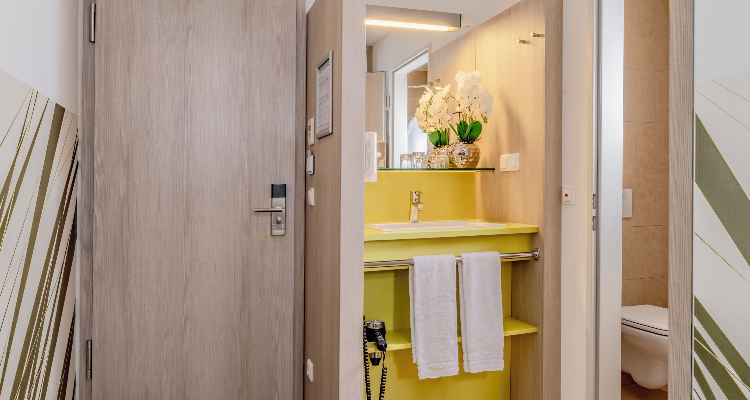 Une salle de bain avec un lavabo jaune, des serviettes blanches, un miroir et des toilettes.