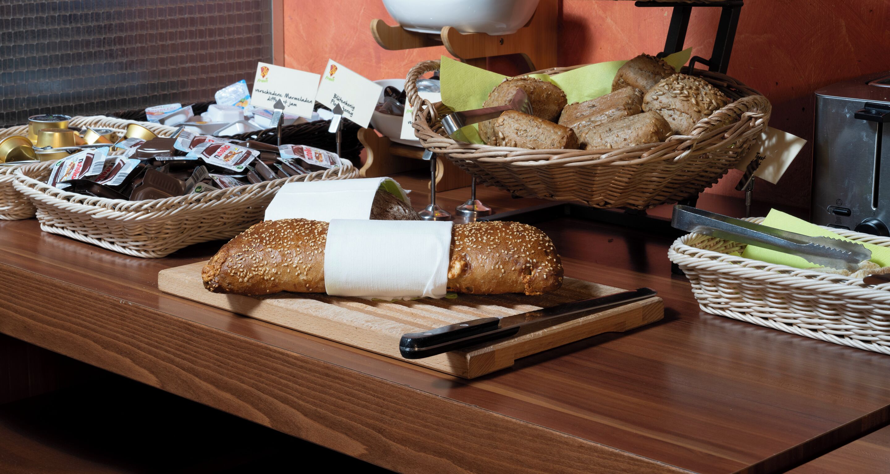Ein Büfett mit verschiedenen Speisen, darunter Brot und Gebäck, sowie ein Messer auf einem Schneidebrett.