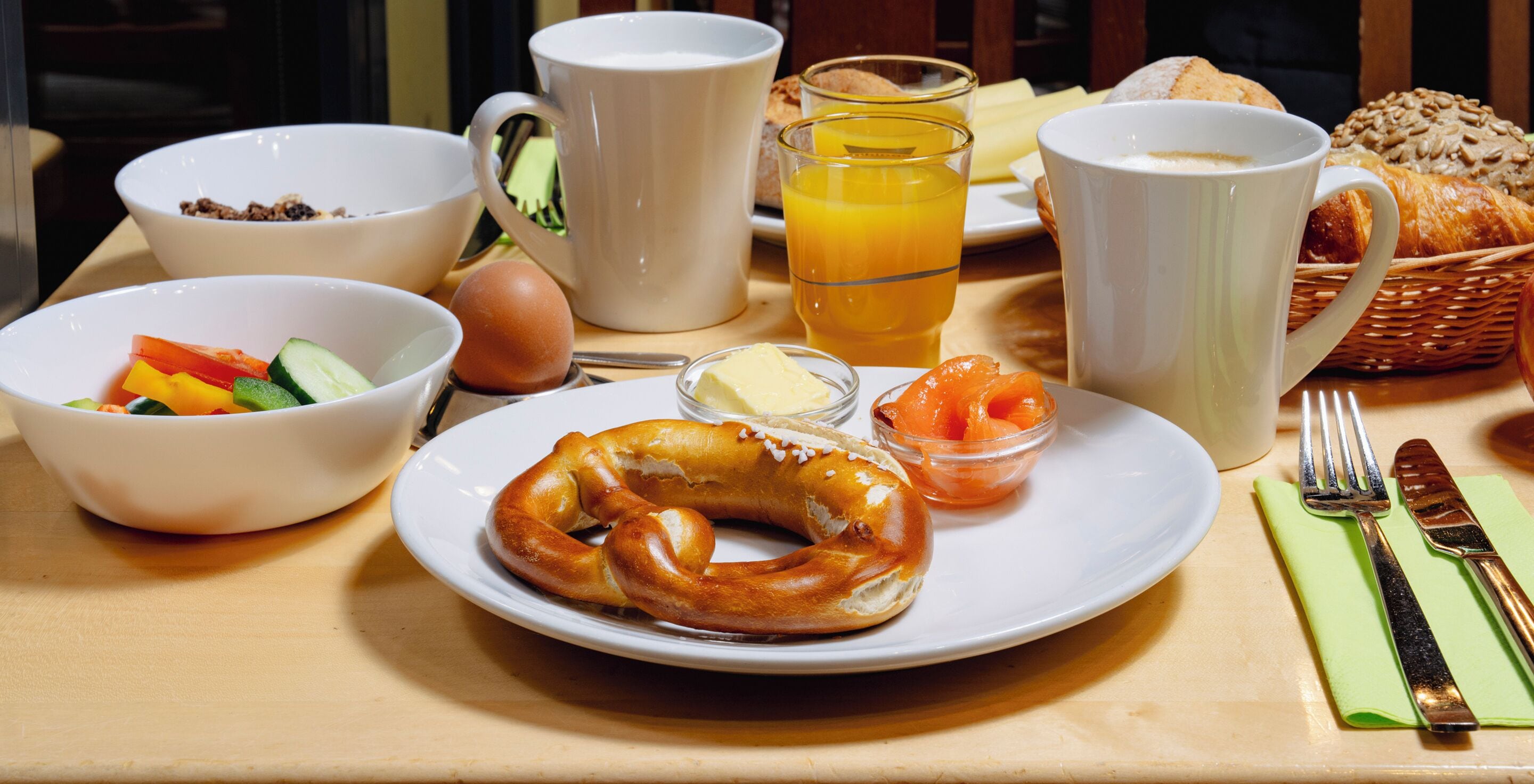 Una mesa de desayuno con un plato de comida, que incluye un pretzel, un bol de fruta y un vaso de jugo de naranja.