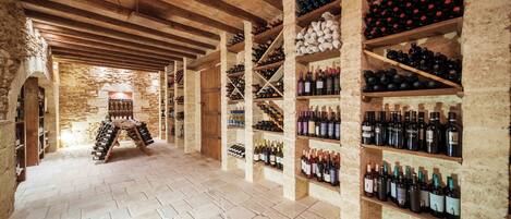 A wine cellar with wooden shelves and stone walls, featuring a variety of wine bottles.