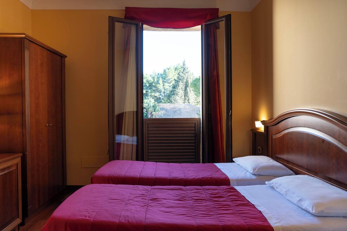 Habitación de hotel con dos camas, cabeceros de madera, un armario y una ventana con cortinas.