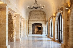 Un couloir aux murs de pierre, doté d’une cheminée et de fenêtres en arc de cercle.