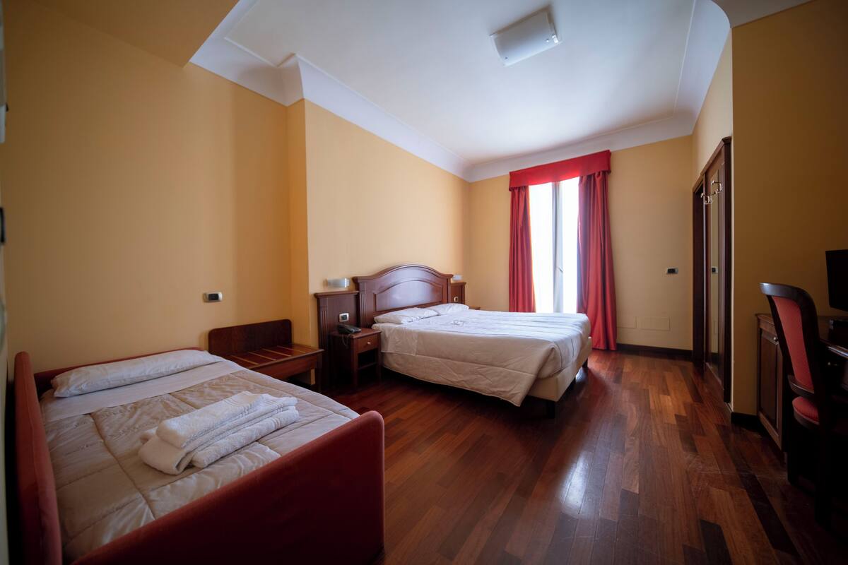 Habitación de hotel con dos camas, suelo de madera, cortina roja y televisor.