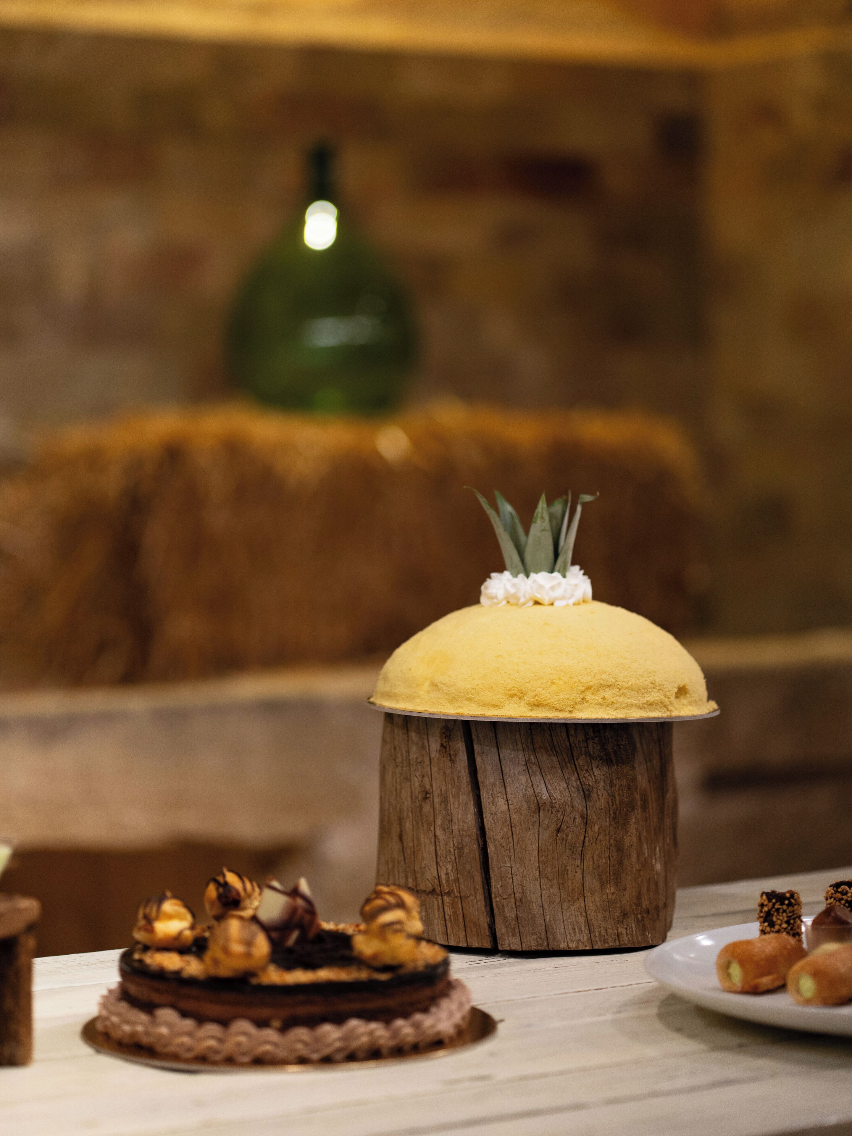 A dessert table with a variety of cakes and pastries, including a yellow cake on a wooden stand and a chocolate cake with nuts.