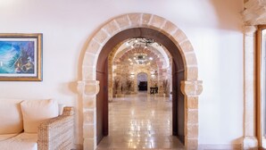 Un pasillo con arcos de piedra, un candelabro, un sofá y un cuadro enmarcado.