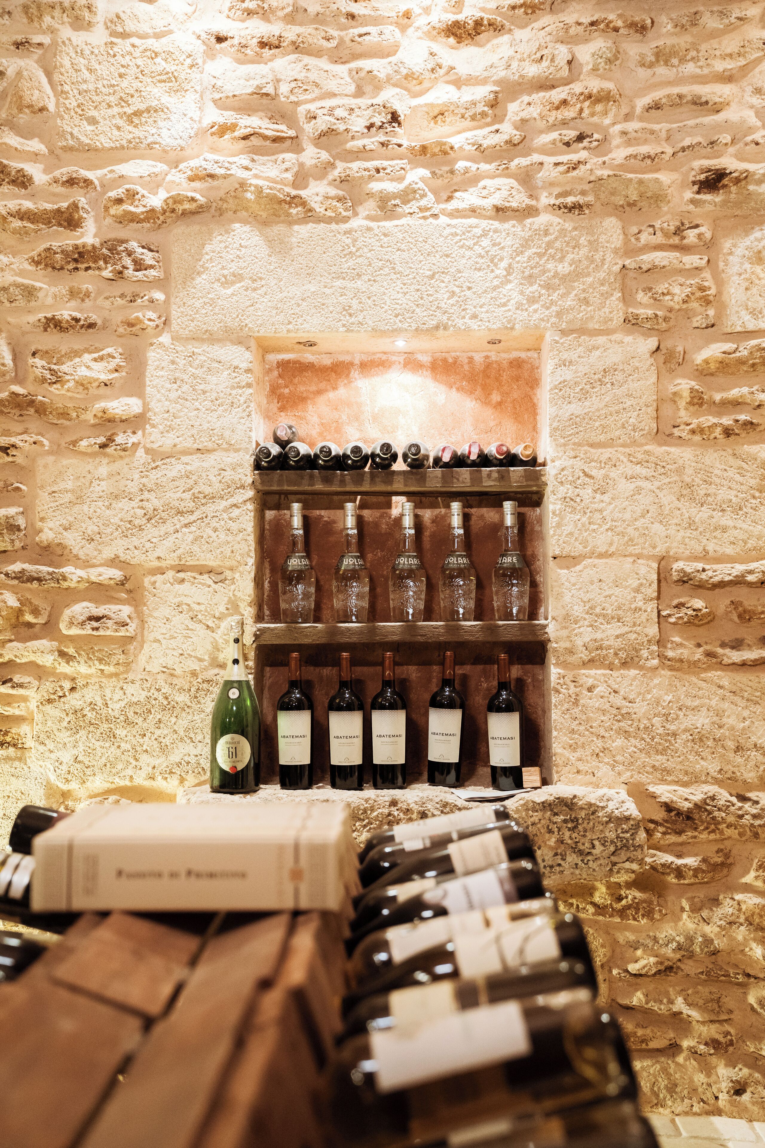 Una bodega con pared de piedra, estanterías de madera y botellas de vino.