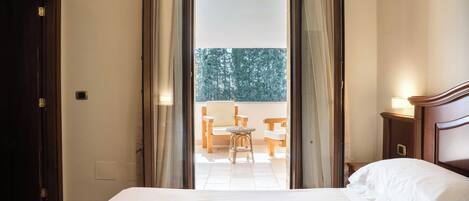 A hotel room with a bed, a nightstand, a window with curtains, and a view of the outside balcony.
