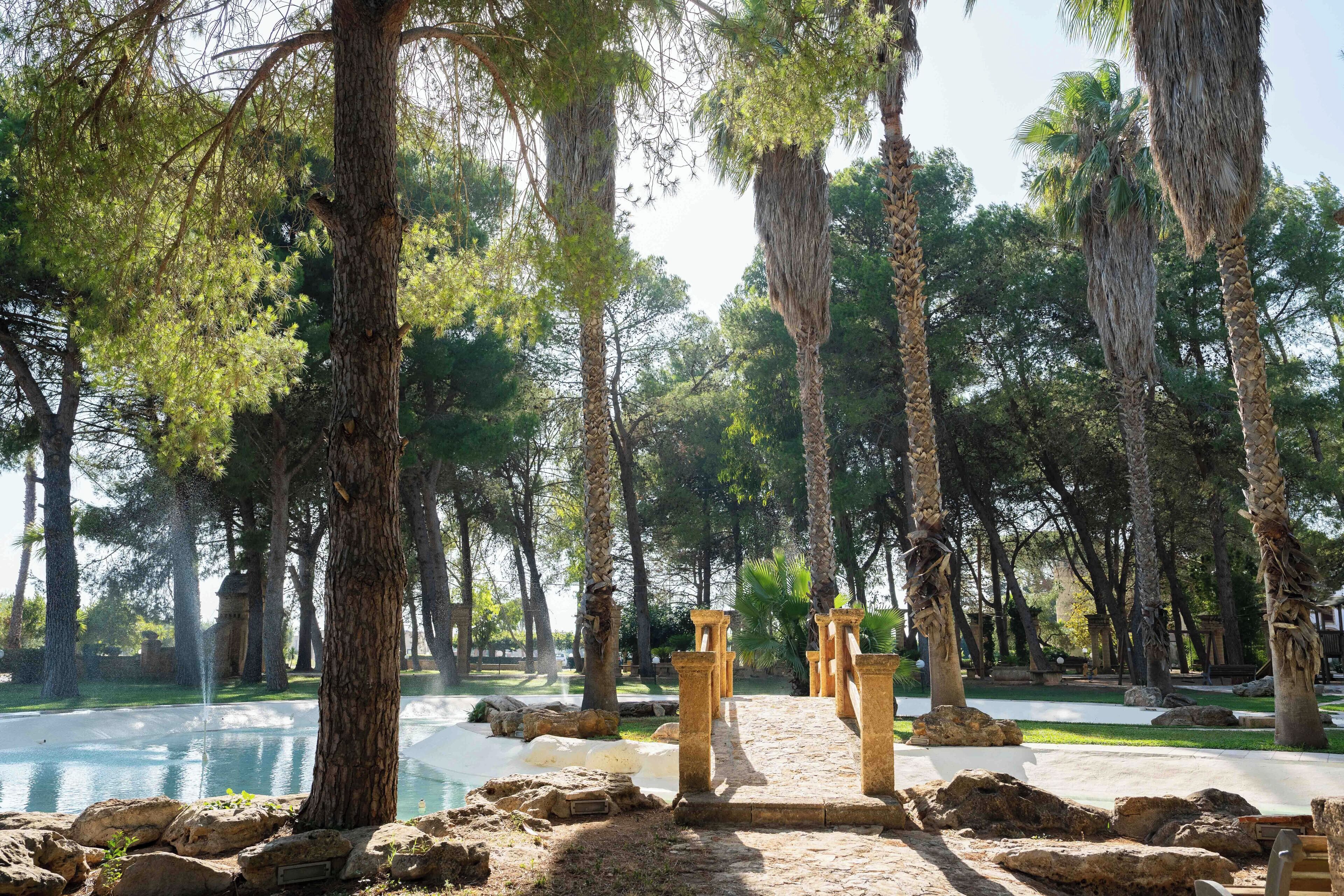 A serene outdoor area with a pool, surrounded by tall trees and stone pillars.