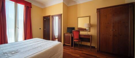 Una habitación de hotel con cama, escritorio, silla, armario y un espejo grande.