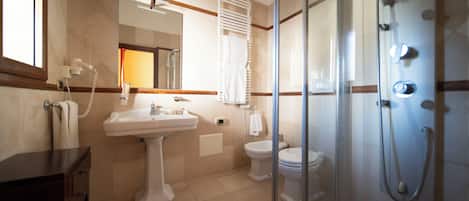 Un baño con lavamanos, dos inodoros, cabina de ducha de vidrio y espejo.