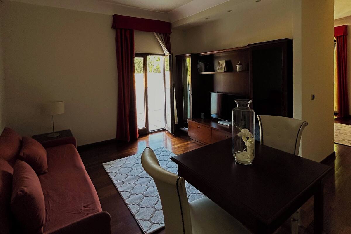 Una sala de estar con sof á, una mesa de comedor con sillas, televisor y una zona de cocina con armarios y microondas.