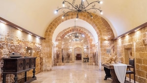 Un pasillo de paredes de piedra con un candelabro, una mesa de madera con mantel blanco y un banco.