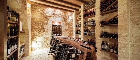 A wine cellar with wooden racks and shelves filled with bottles, stone walls, and a wooden ceiling.