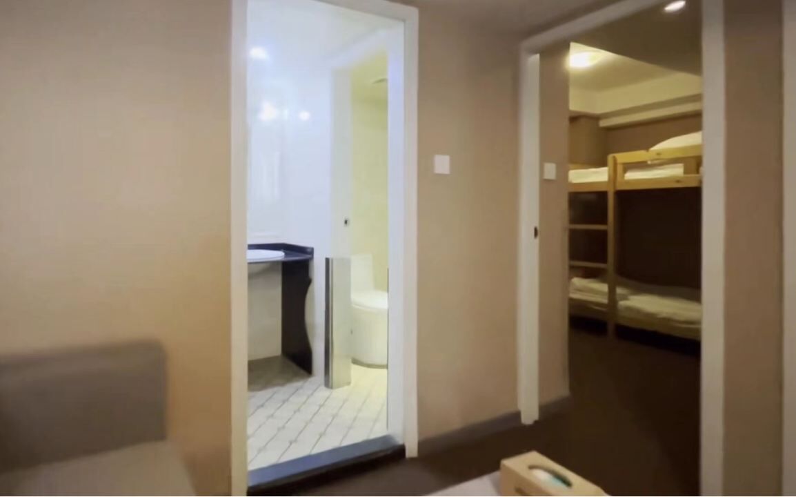 Une chambre avec un lit superposé, un petit bureau et une porte blanche donnant sur une salle de bain.