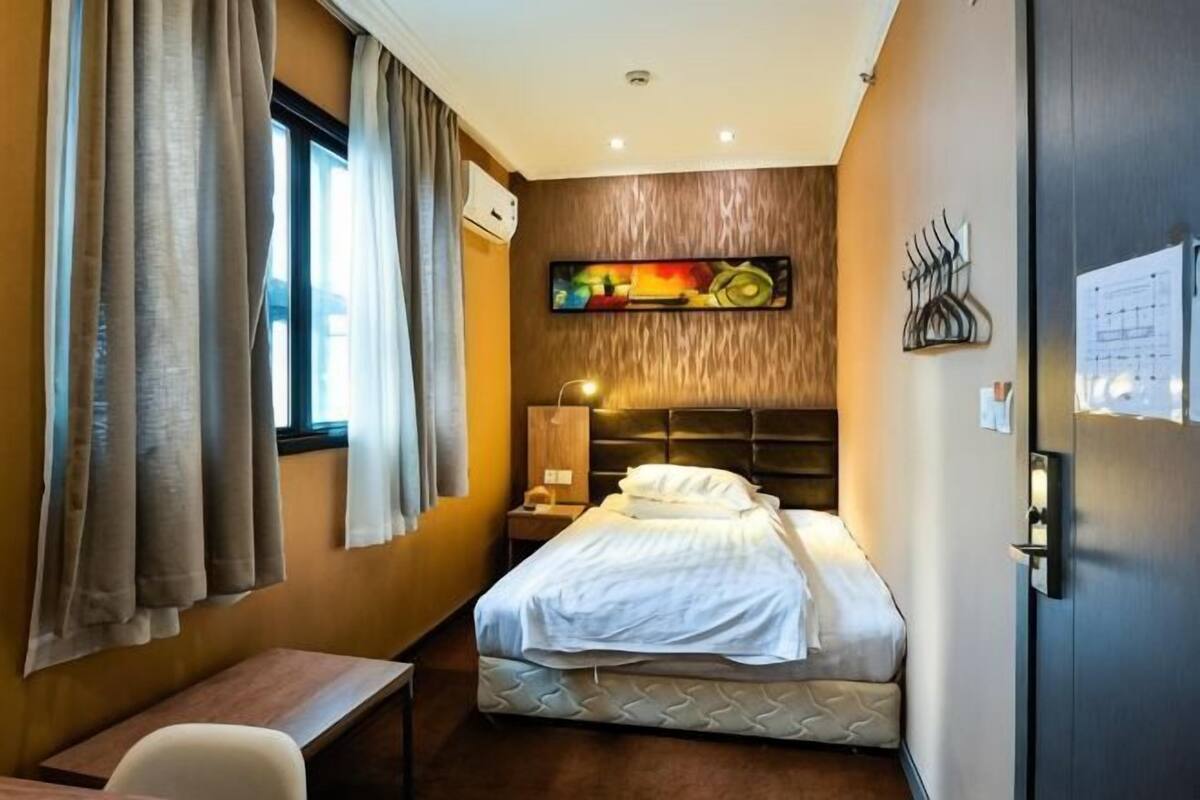 A hotel room with a bed, bedside table, lamp, and a painting on the wall.