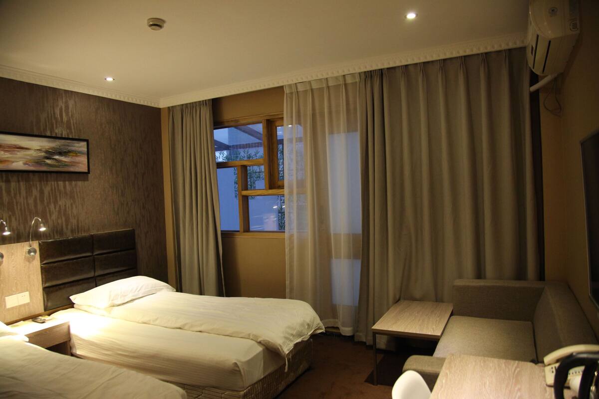 A hotel room with two beds, a sofa, a desk, and a window with curtains.