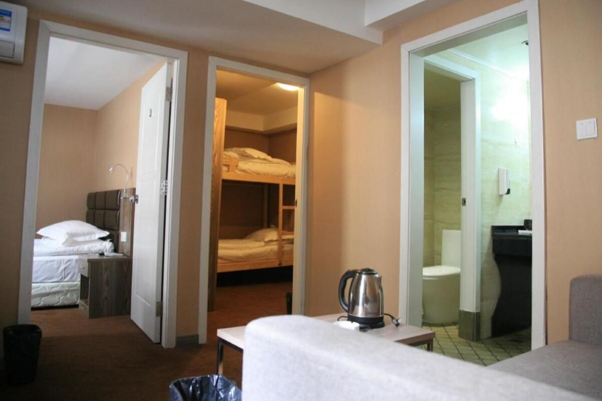 A hotel room with a bed, a table with a kettle, a bathroom with a toilet, and a shower area.